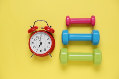 Alarm clock and dumbbells on yellow background, flat lay. Morning exercise