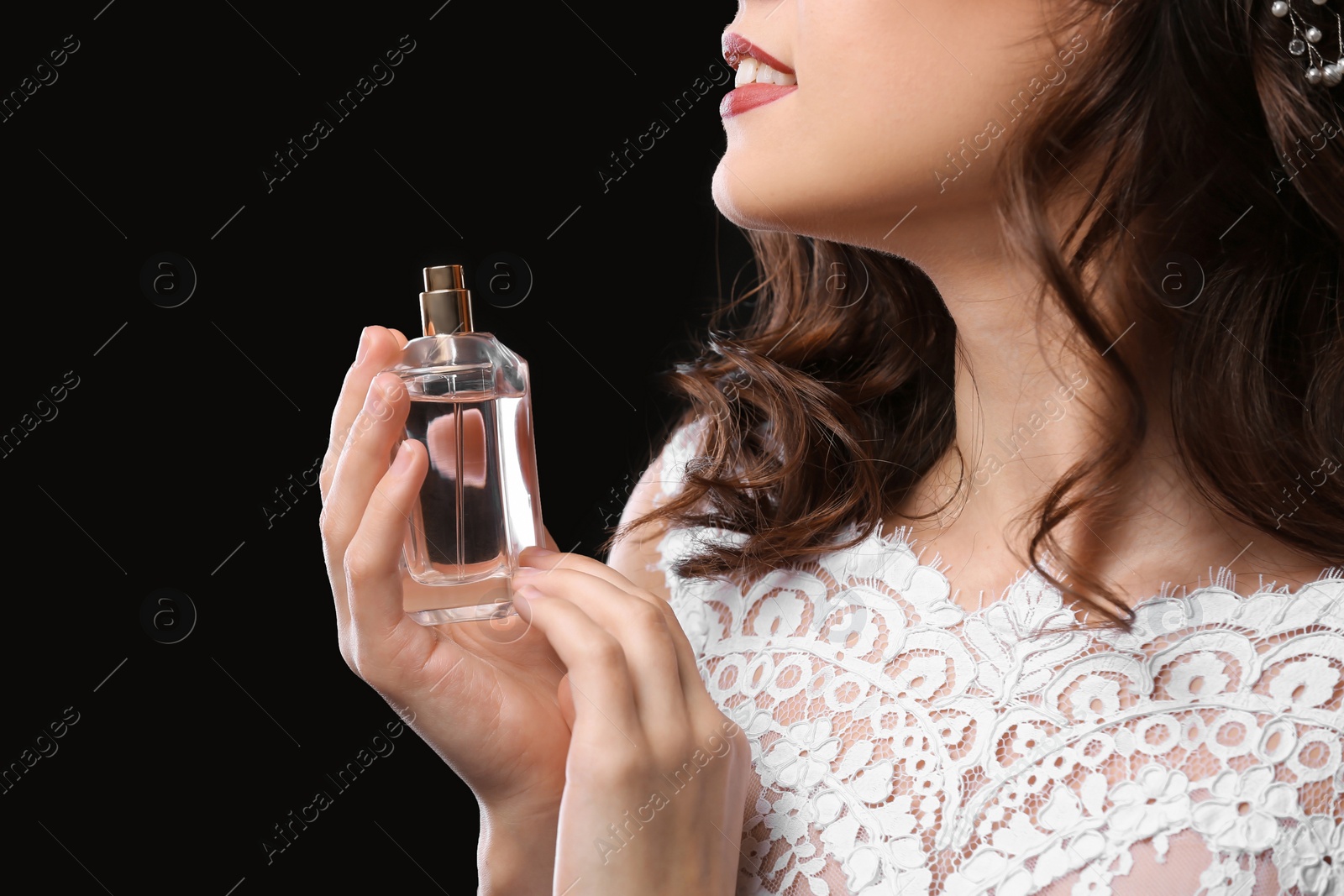 Photo of Beautiful young bride with bottle of perfume on black background, closeup