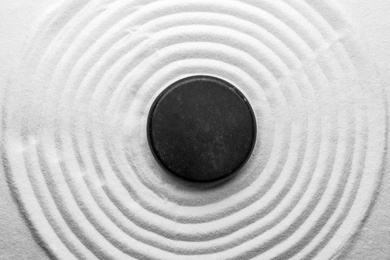 Photo of Black stone on sand with pattern, top view. Zen, meditation, harmony
