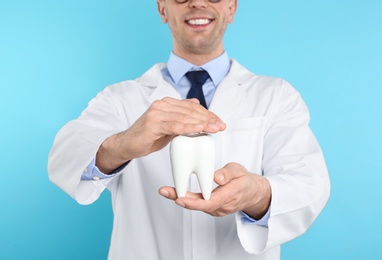 Photo of Male dentist holding tooth model on color background, closeup
