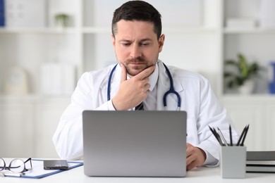 Photo of Doctor having online consultation via laptop at table in clinic