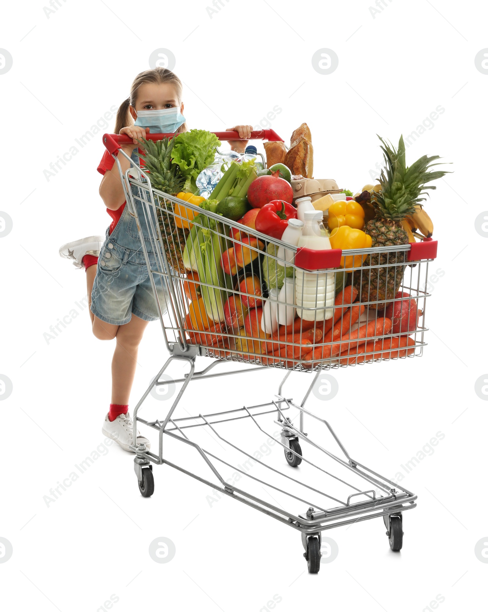 Photo of Little girl in medical mask with shopping cart full of groceries on white background