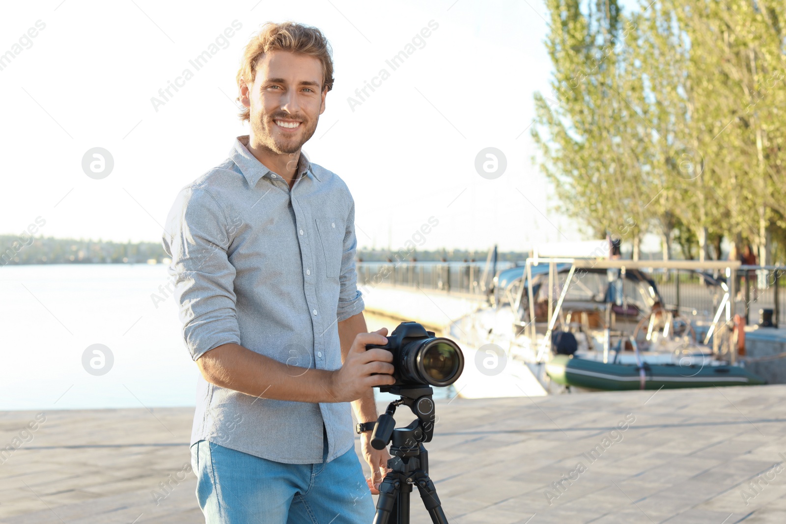 Photo of Young male photographer standing with professional camera at pier. Space for text