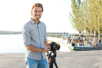 Young male photographer standing with professional camera at pier. Space for text