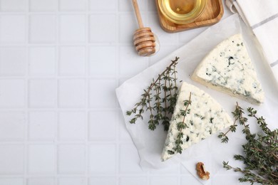 Tasty blue cheese with thyme and honey on white tiled table, flat lay. Space for text