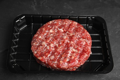 Photo of Plastic container with raw meat cutlet for burger on black table