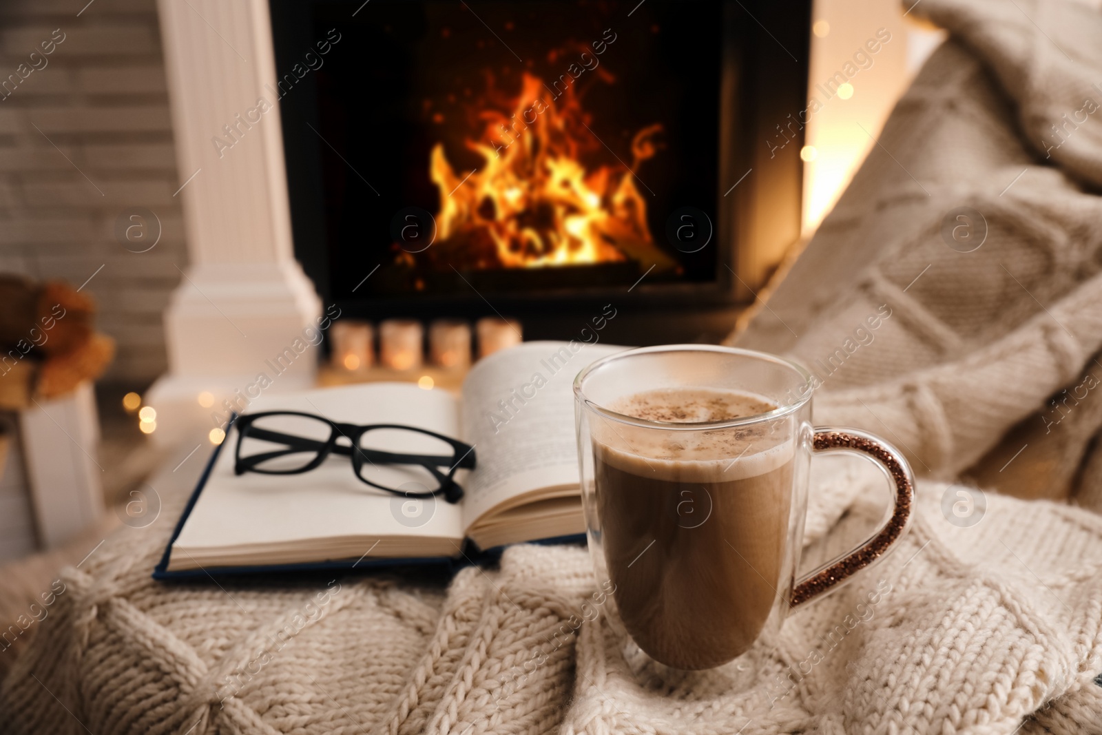 Photo of Cup of coffee, book and glasses near fireplace indoors, space for text. Cozy atmosphere