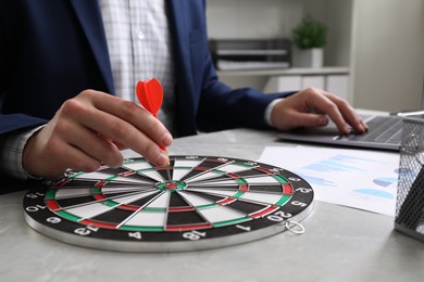 Business targeting concept. Man with dart aiming at dartboard at gray table indoors, closeup