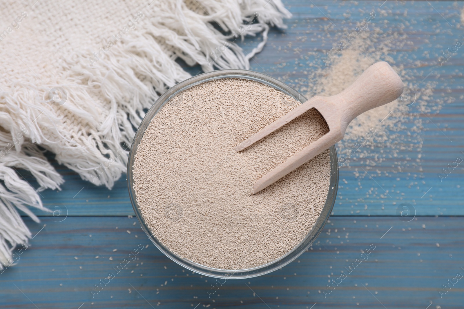 Photo of Bowl and scoop with active dry yeast on light blue wooden table, top view