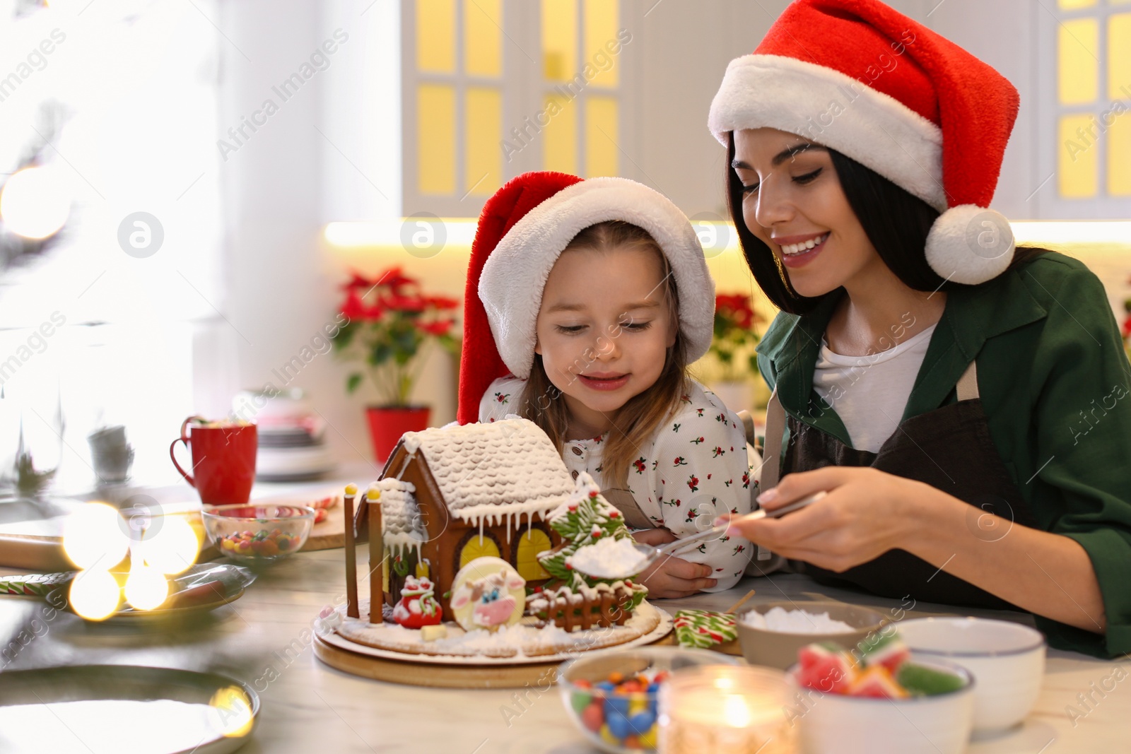 Photo of Mother and daughter decorating gingerbread house at table indoors