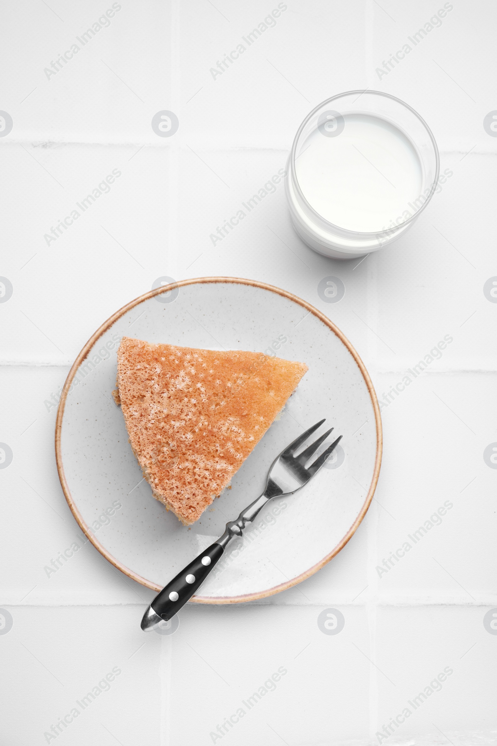 Photo of Piece of tasty sponge cake served with milk on white tiled table, flat lay