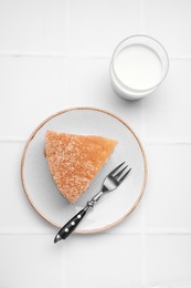 Piece of tasty sponge cake served with milk on white tiled table, flat lay