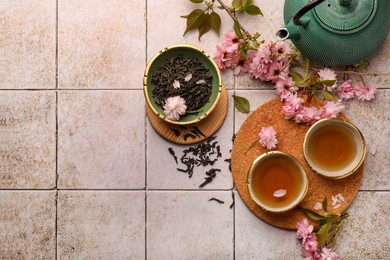 Traditional ceremony. Cup of brewed tea, teapot, dried leaves and sakura flowers on tiled table, flat lay with space for text