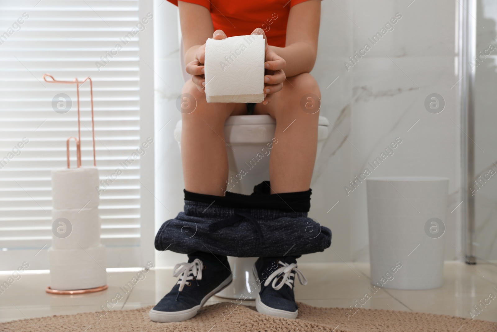 Photo of Boy with paper suffering from hemorrhoid on toilet bowl in rest room, closeup