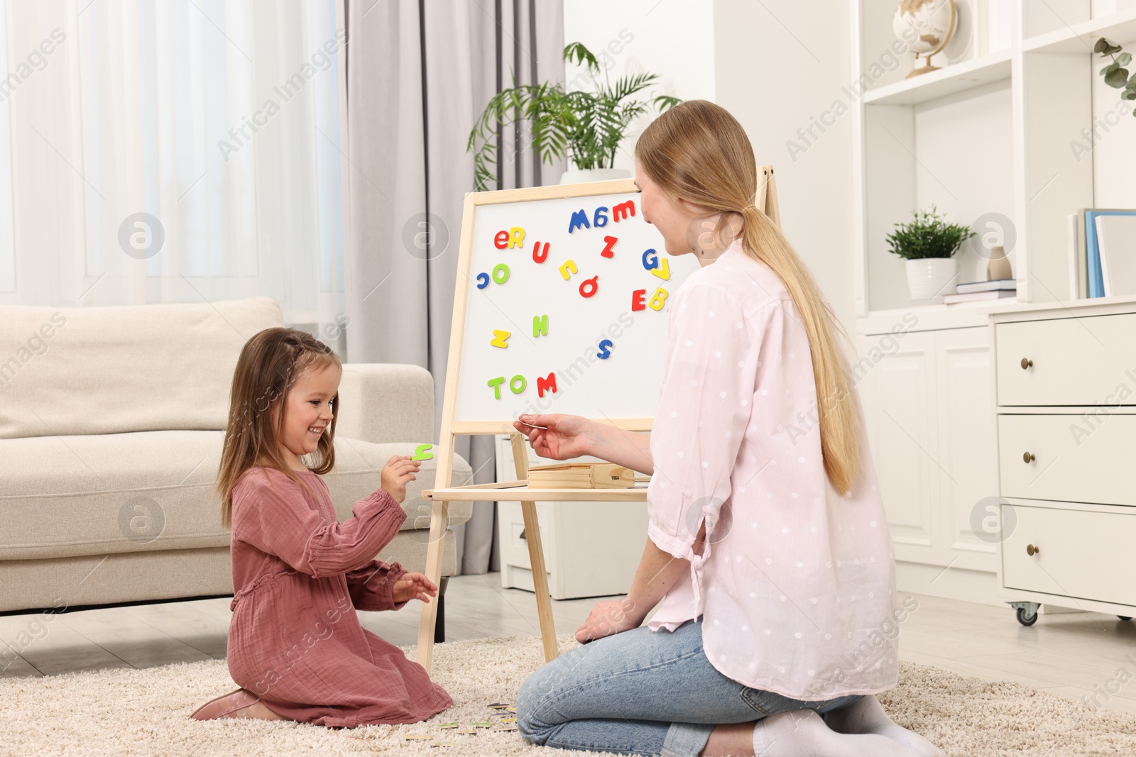 Photo of Mom teaching her daughter alphabet with magnetic letters at home