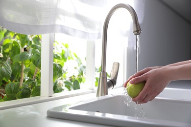 Photo of Woman washing apple over sink in kitchen, closeup. Space for text