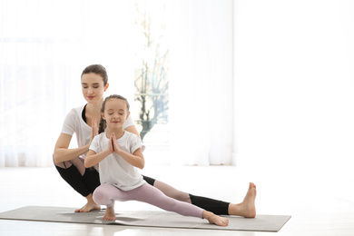 Young mother with little daughter practicing yoga at home