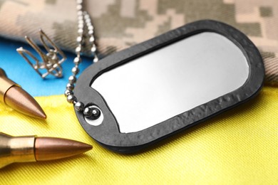 Photo of Military ID tag near Ukrainian trident, bullets and camouflage fabric on national flag of Ukraine, closeup