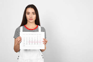 Photo of Young woman holding calendar with marked menstrual cycle days on light background. Space for text