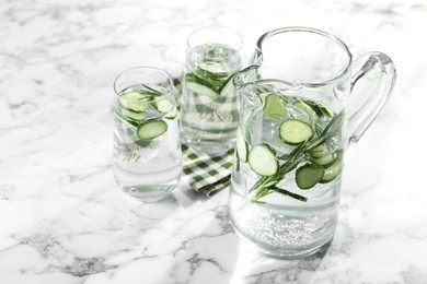 Refreshing cucumber water with rosemary in jug and glasses on white marble table