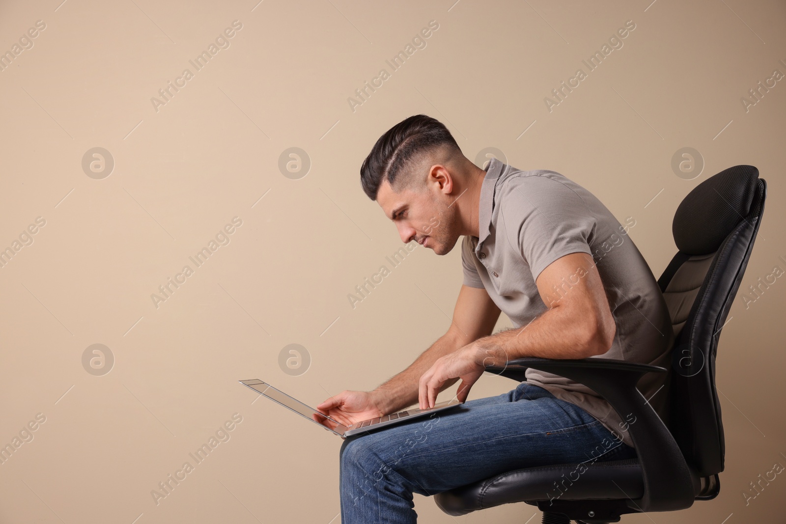 Photo of Man with poor posture using laptop while sitting on chair against beige background, space for text