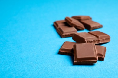 Photo of Pieces of delicious chocolate bar on light blue background. Space for text