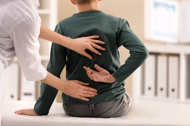 Chiropractor examining child with back pain in clinic, closeup