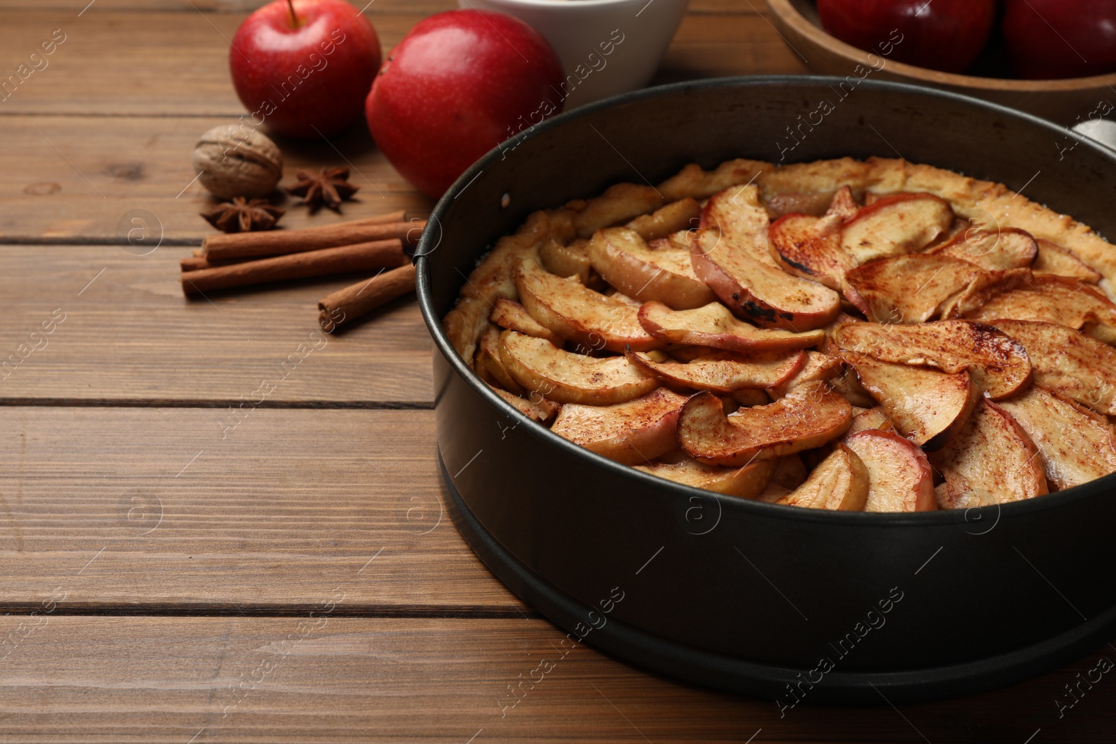 Photo of Delicious apple pie and ingredients on wooden table. Space for text