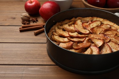 Photo of Delicious apple pie and ingredients on wooden table. Space for text