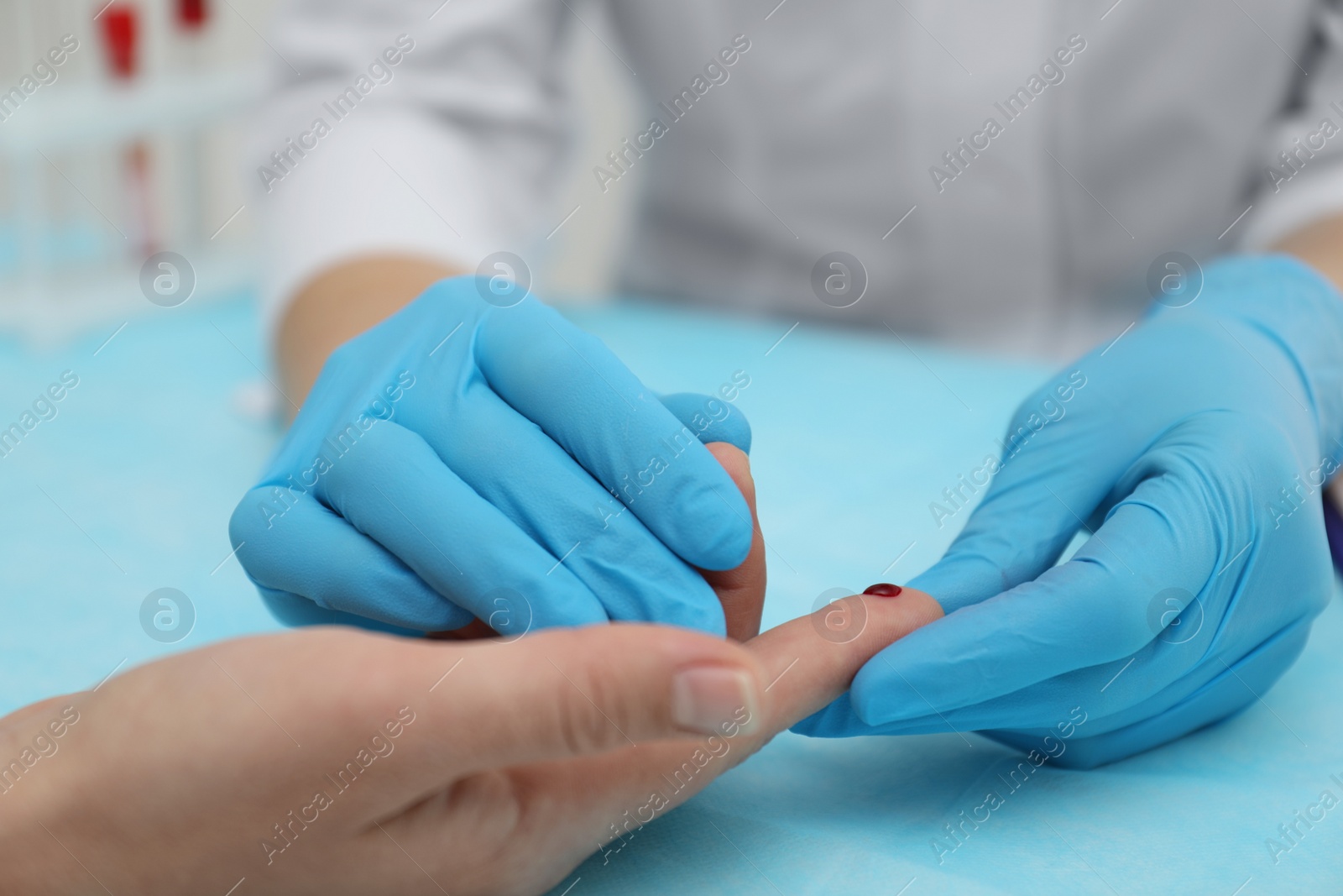 Photo of Doctor taking blood sample from patient's finger at table, closeup