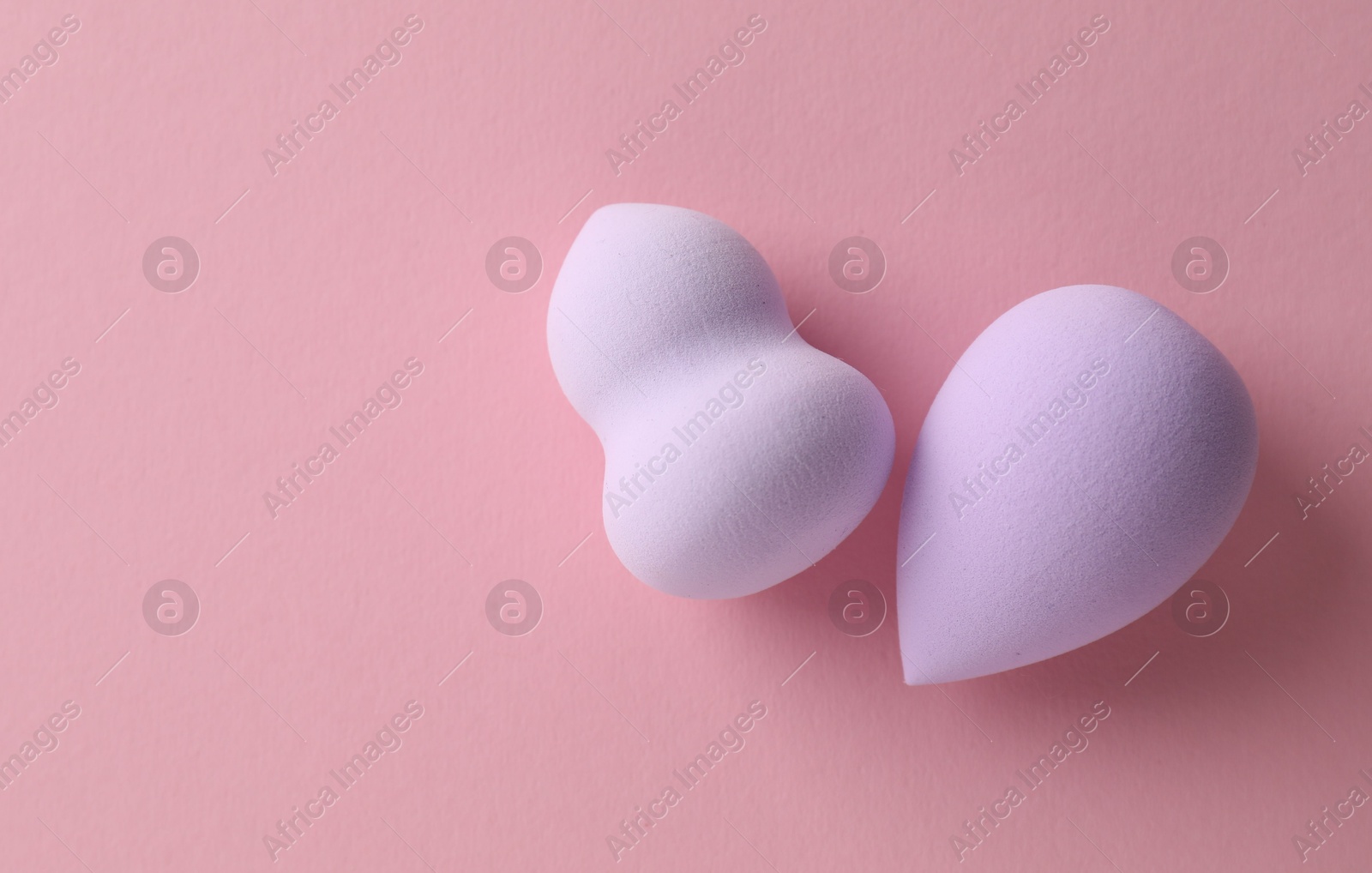 Photo of Two violet makeup sponges on pink background, top view. Space for text