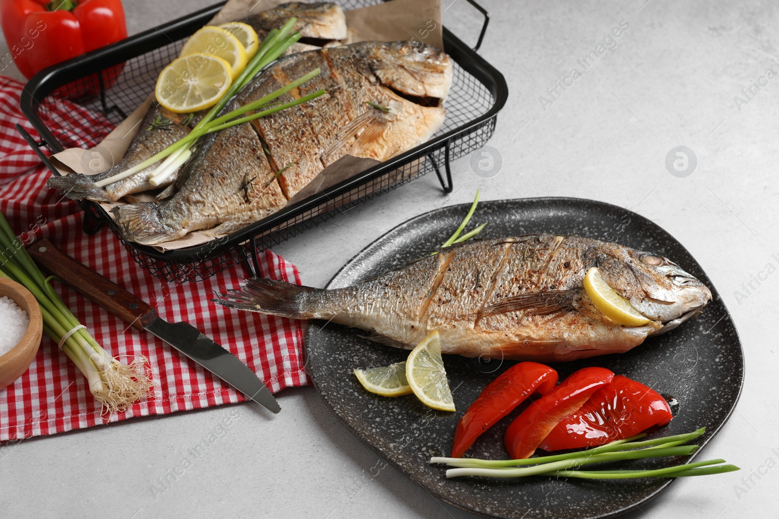 Photo of Delicious baked fish served with green onion, bell pepper and lemon on light textured table. Seafood