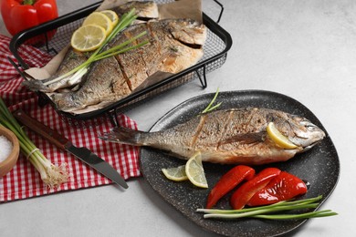Delicious baked fish served with green onion, bell pepper and lemon on light textured table. Seafood