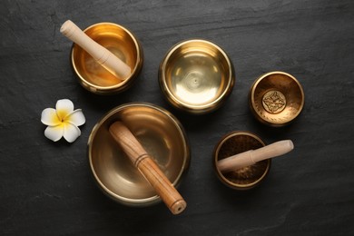 Photo of Golden singing bowls, mallets and flower on black table, flat lay
