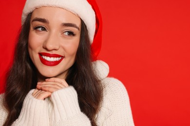 Photo of Christmas celebration. Beautiful young woman in Santa hat on red background, closeup and space for text