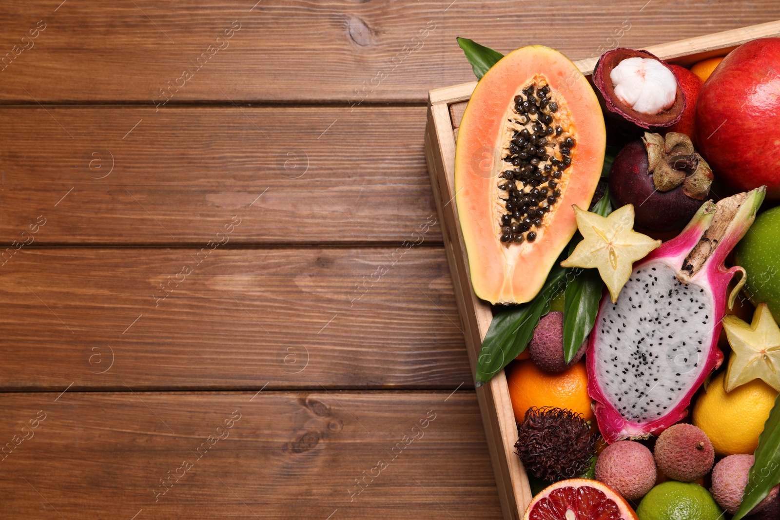 Photo of Crate with different exotic fruits on wooden table, above view. Space for text