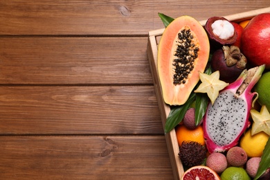 Crate with different exotic fruits on wooden table, above view. Space for text