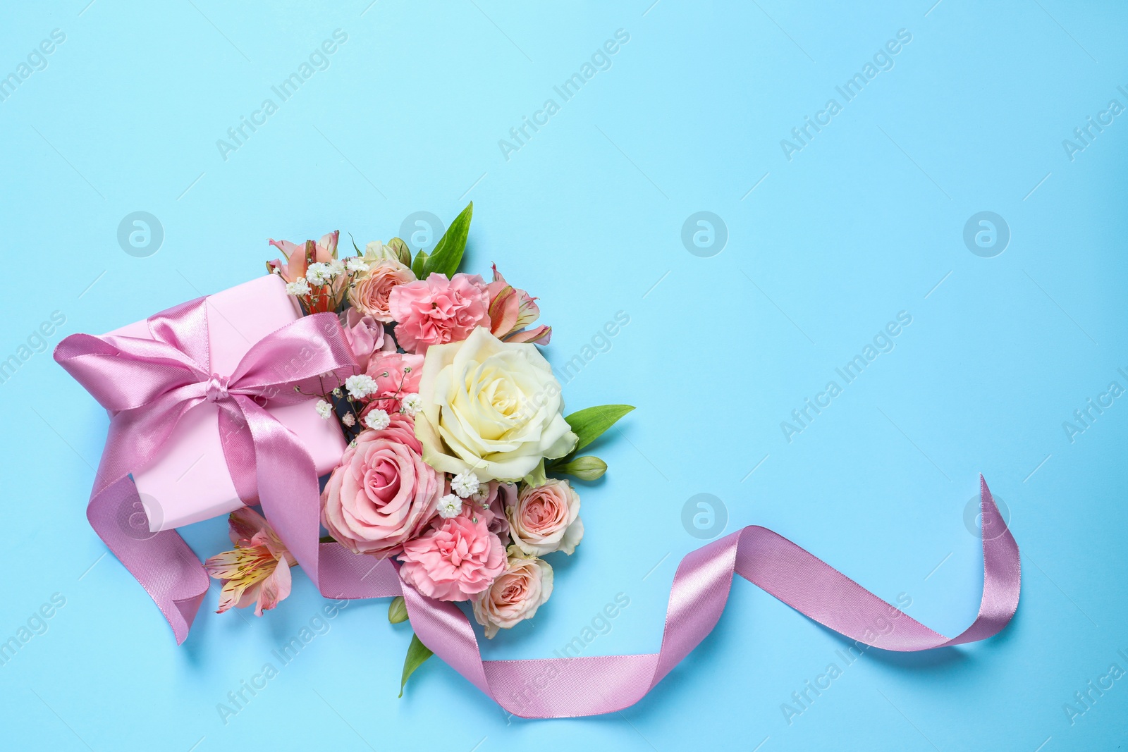 Photo of Gift box and beautiful flowers on light blue background, flat lay. Space for text