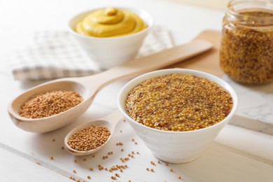 Photo of Bowl and spoons of whole grain mustard on white wooden table