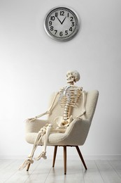 Waiting concept. Human skeleton sitting in armchair indoors