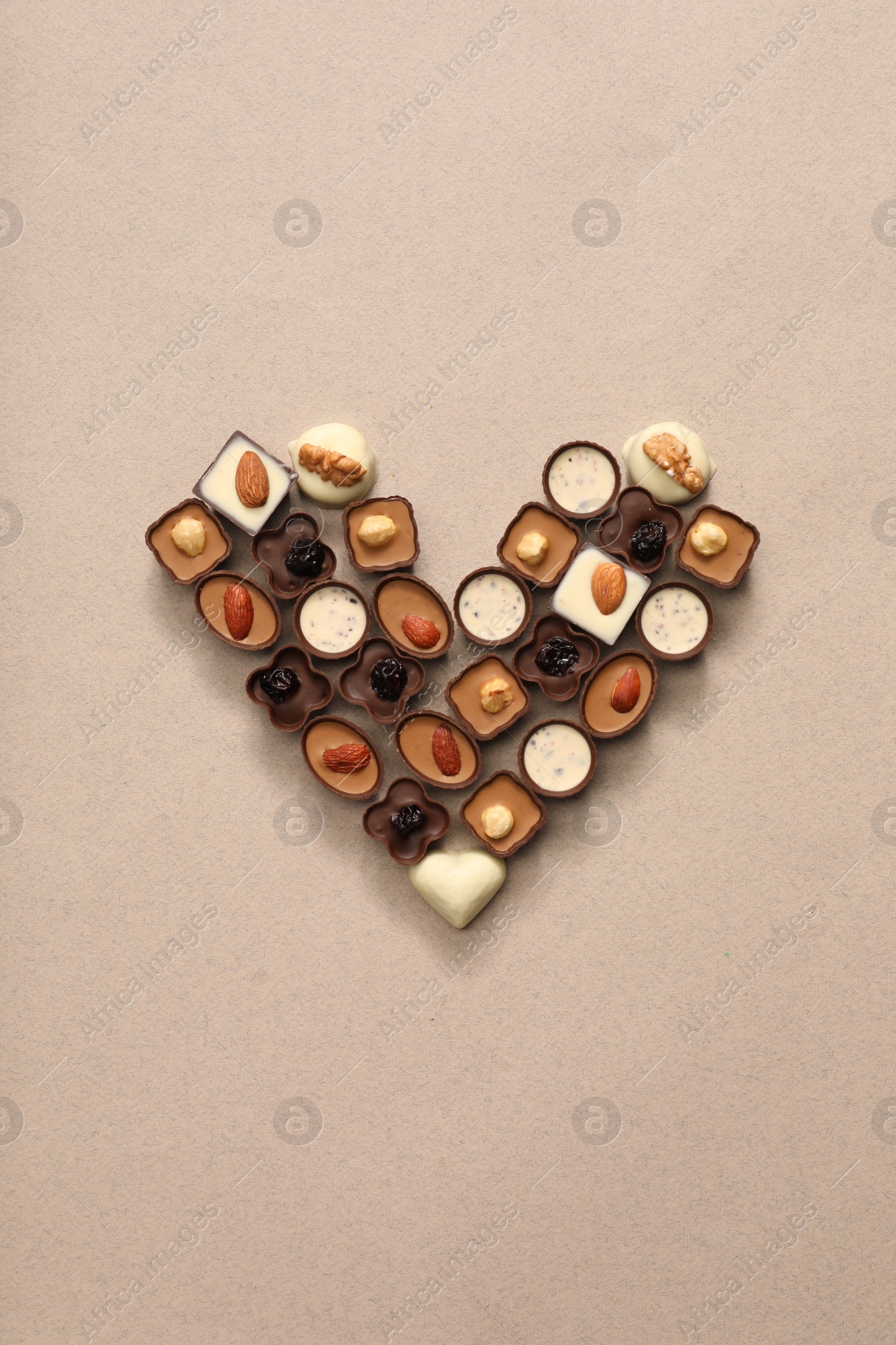 Photo of Heart made with delicious chocolate candies on beige background, top view