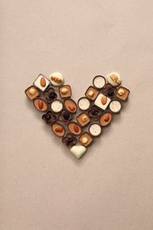 Heart made with delicious chocolate candies on beige background, top view