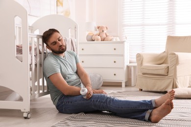 Photo of Tired father with bottle of milk sleeping on floor in children's room