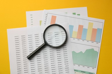 Photo of Accounting documents and magnifying glass on yellow background, top view