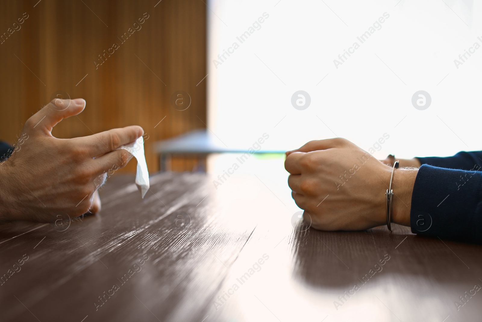 Photo of Police officer interrogating drug dealer in handcuffs at desk indoors. Criminal law