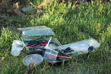 Photo of Used plastic tableware on grass outdoors, space for text. Environmental pollution concept