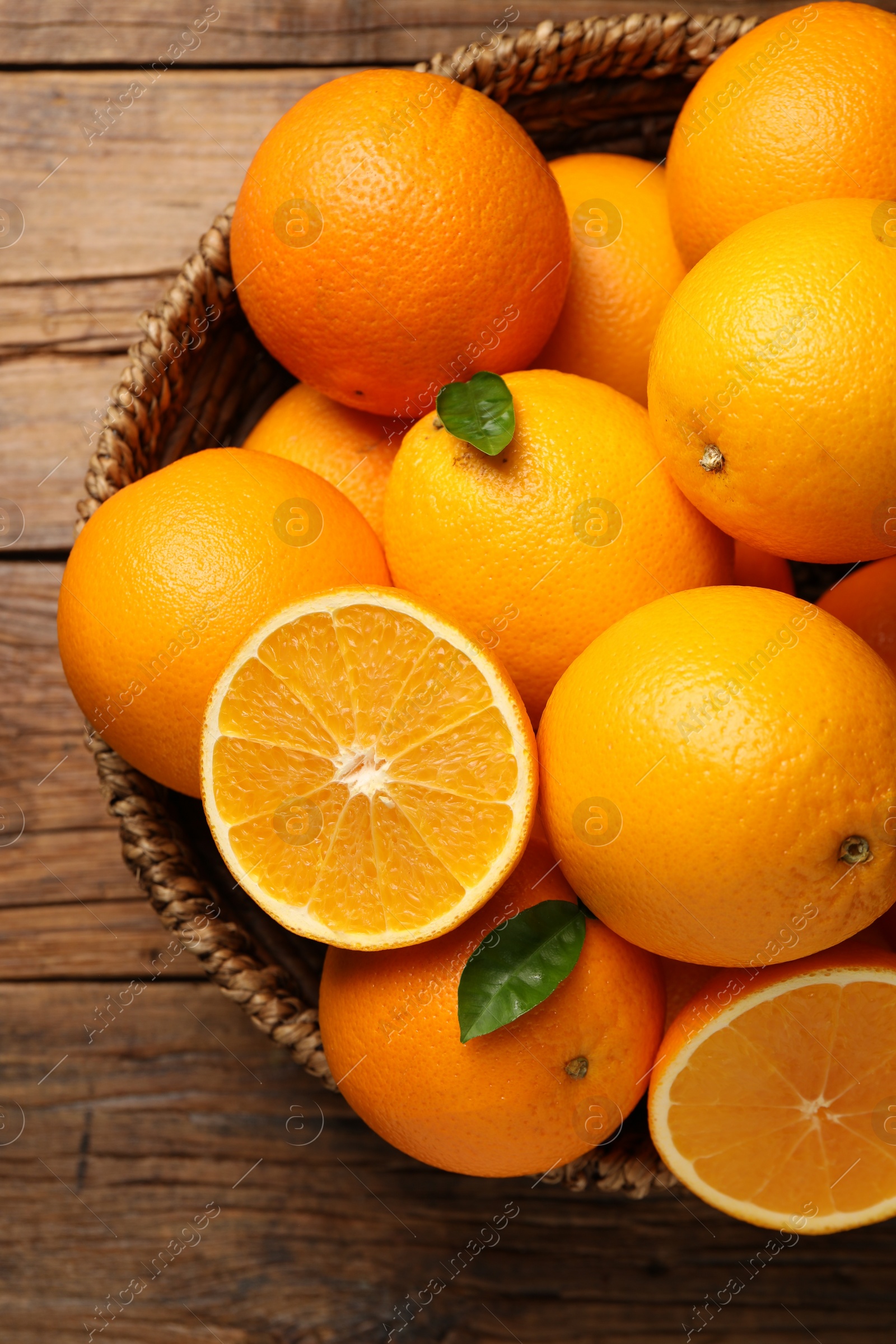 Photo of Many ripe oranges and green leaves on wooden table, top view