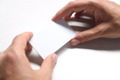 Man holding blank cards at white table, closeup. Mockup for design