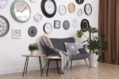Photo of Stylish room interior with comfortable furniture, beautiful houseplant and collection of different clocks on white wall