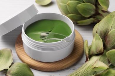 Photo of Package of under eye patches and artichokes on white wooden table, closeup. Cosmetic product